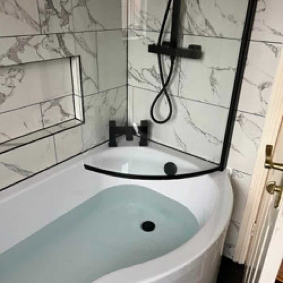 Image of modern bathroom with white mottled tiles and bathtub with matt black fittings installed by Plumb Yorkshire Ltd.