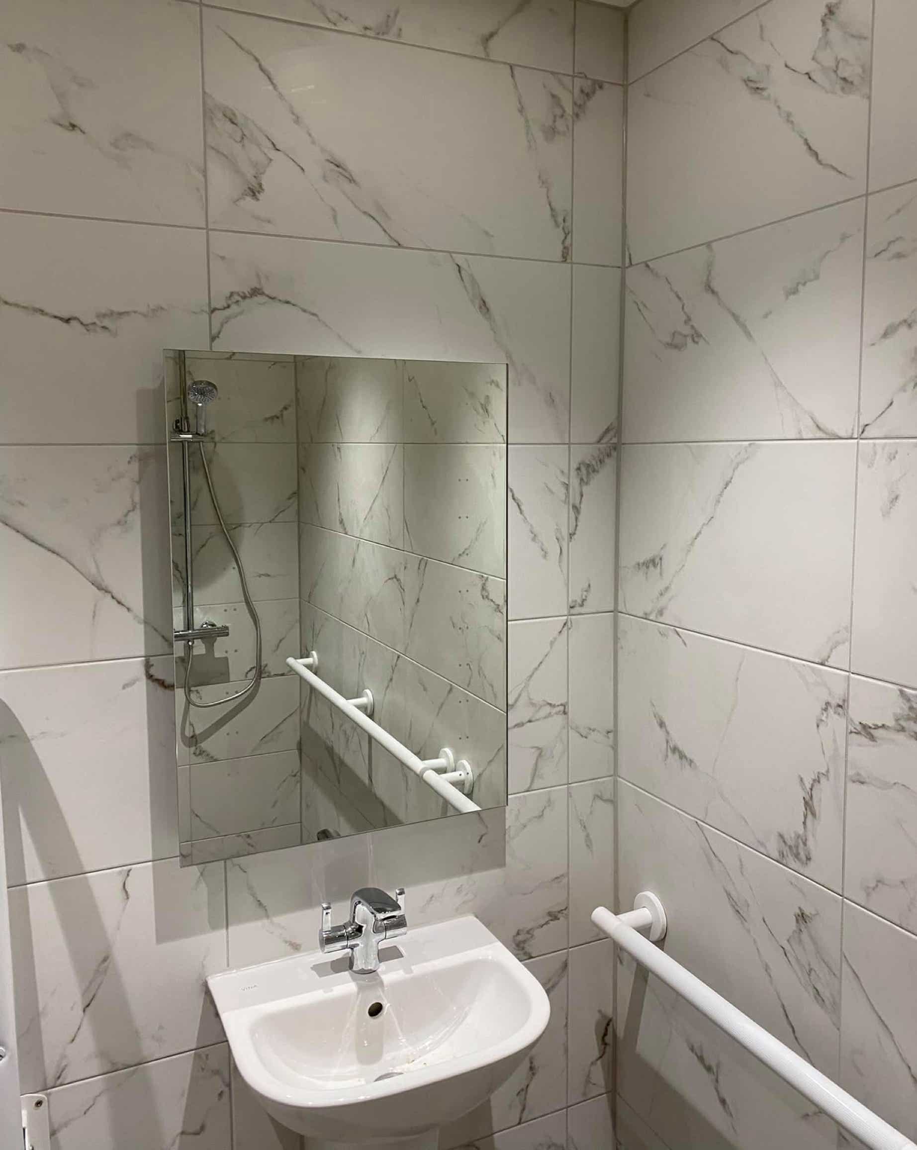 Image of sink with mirror with white tiles with flecks of grey in a mobility bathroom created by Plumb Yorkshire Ltd.