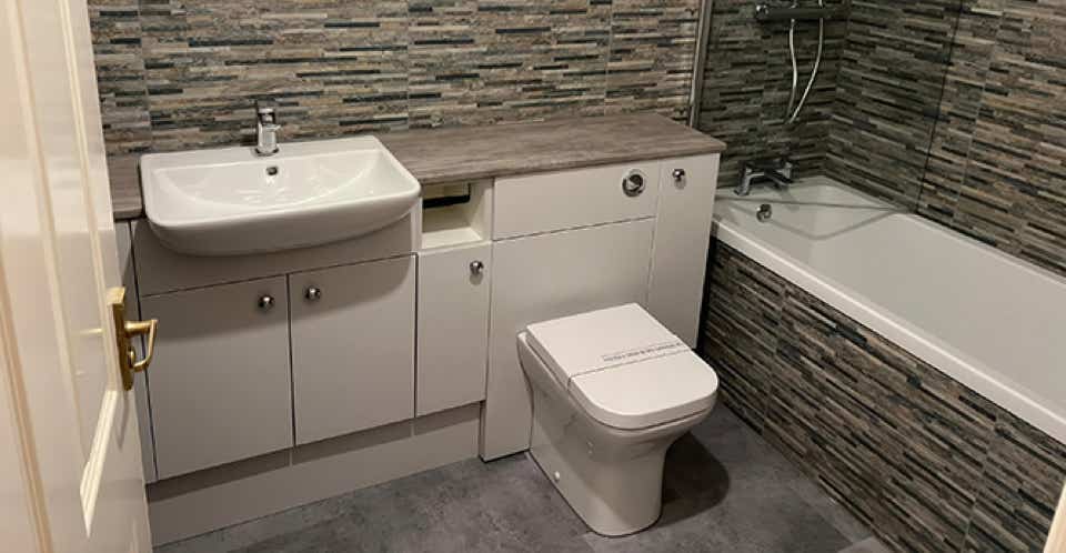 Image of a modern white and beige bathroom with stone effect tiling, white furniture and silver fittings.