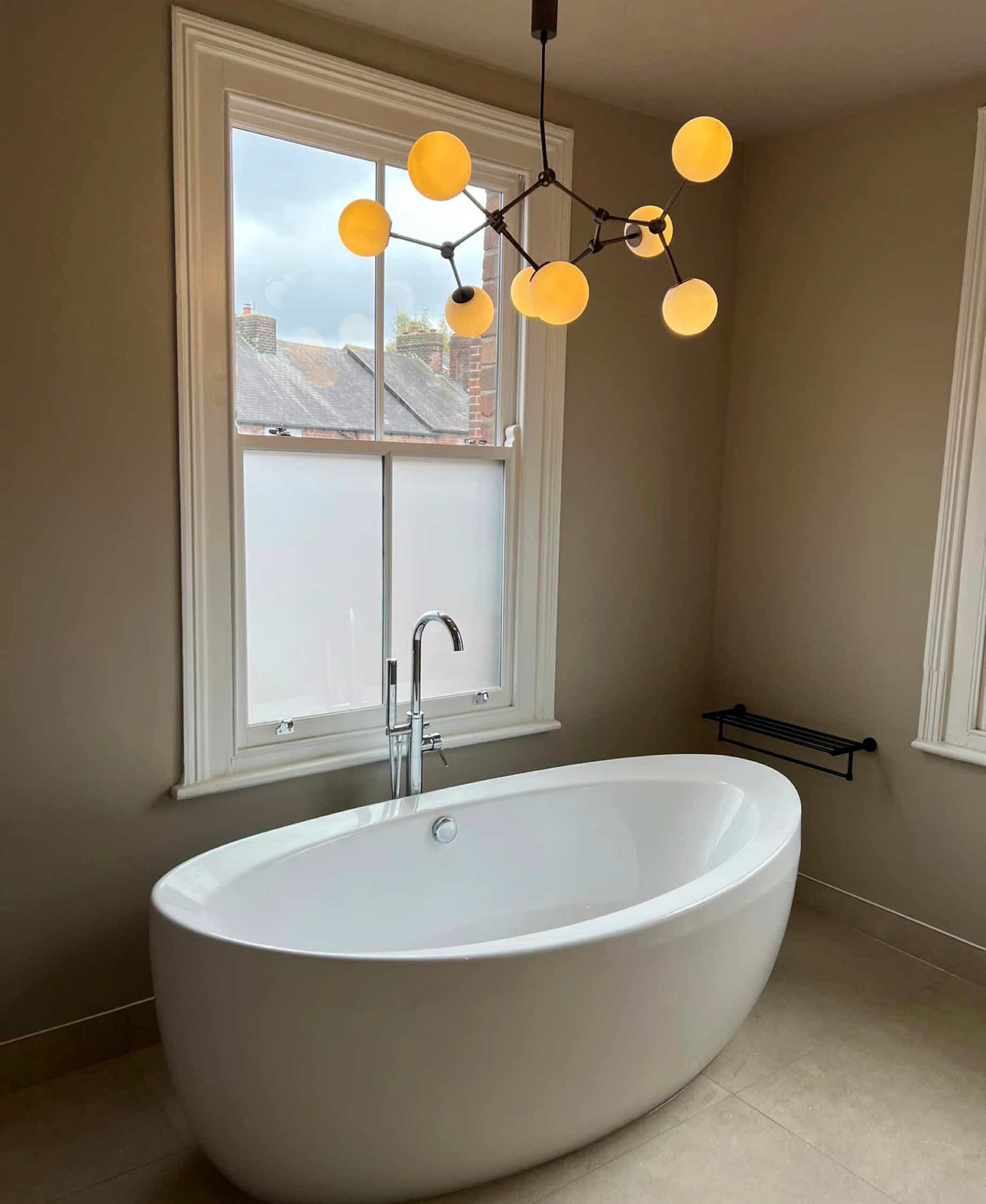 Modern free-standing bath under molecule design lighting in a beige bathroom fitted by Plumb Yorkshire Ltd.
