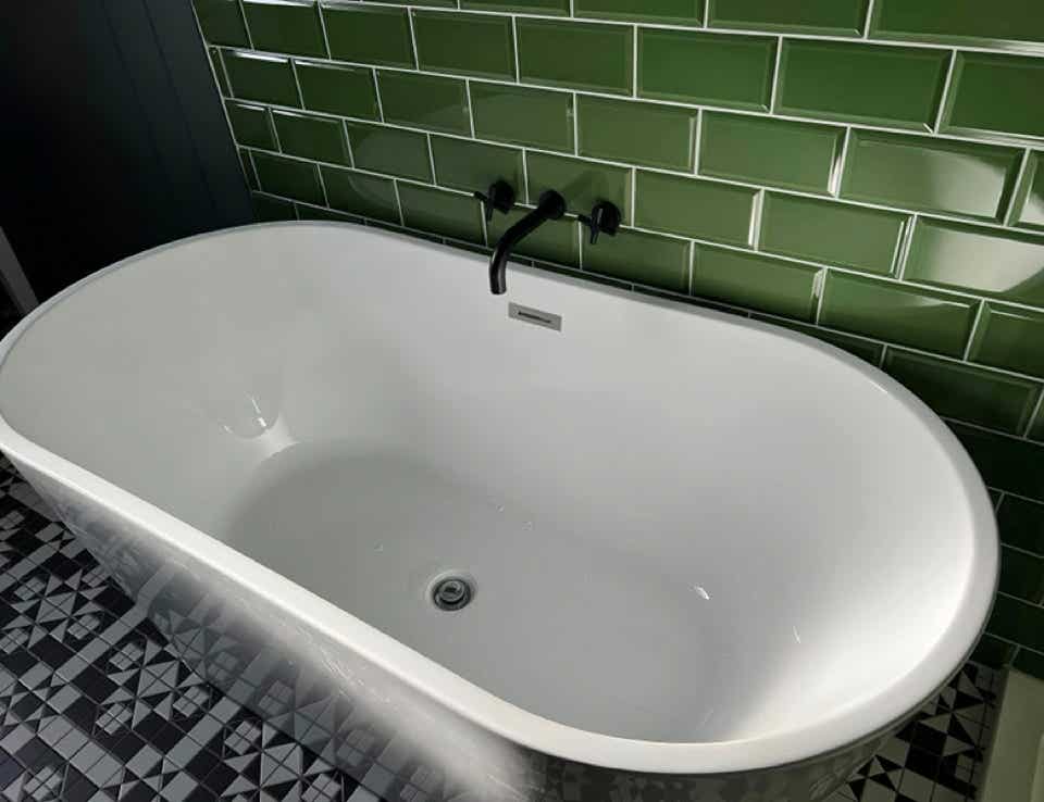 A modern bath tub at the side of fern green tiles.